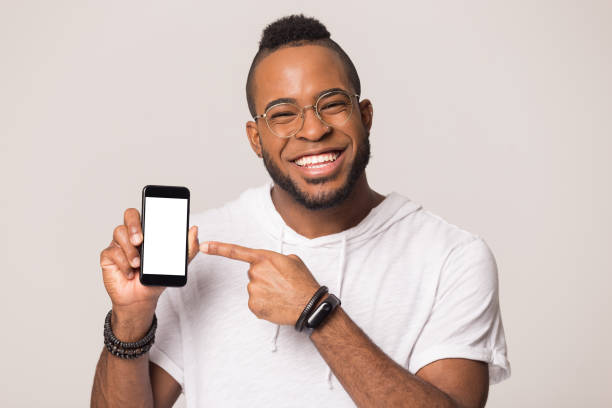 istock Smiling black man look at camera point at smartphone screen 1262402142
