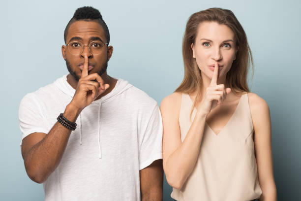 istock Diverse man and woman hold finger on lips telling secret 1262403304