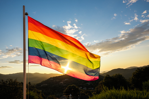 The rising sun shines brightly through a multicolored rainbow flag