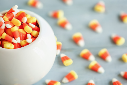 Halloween holiday candy corn in a white bowl over a blue wooden background for Trick or Treat.