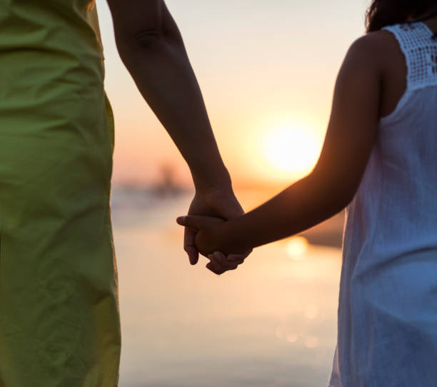 istock Mother and daughter walking on beach at sunset closeup 1262410442
