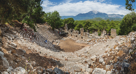Phaselis, Turkey - May 19, 2018. Tourists walk into ruins of amphitheatre of ancient Phaselis city. Panorama view on famous architectural landmark, Kemer district, Antalya province.