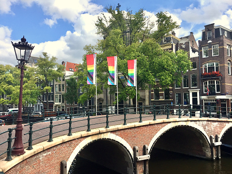 Rainbow colored flags, bridge and traditional Amsterdam houses at canal