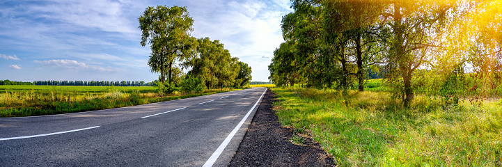 Empty asphalt road in countryside, left bend of road, fields at blue sky and clouds background