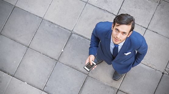 Business man with mobile phone standing on square, seen in top view