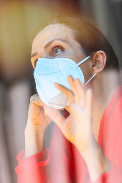 istock Concerned unemployed mature woman looking through a window wearing a protective face mask 1262449863
