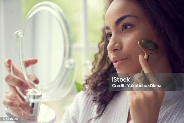 Young Woman Using Jade Roller At Home Stock Photo - Download Image Now - Jade Roller, Human Face, Massaging