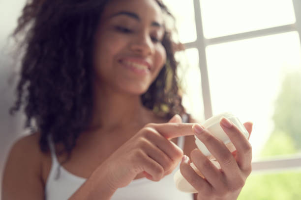 istock Smiling young female using moisturizing cream at home 1262451336