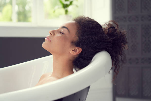 Smiling curly woman having rest in bathroom Calm pretty young female is lying while having bath and closing eyes for deep relaxation bathtub stock pictures, royalty-free photos & images