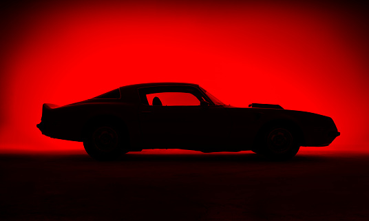 Silhouette of an old fashion muscle car on a red background.