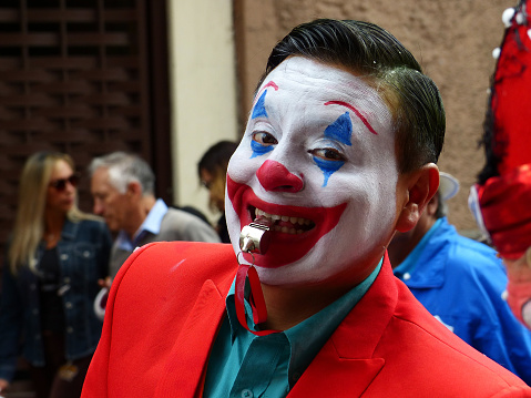 Cuenca, Ecuador - February 22, 2020: Parade during Carnival at historical center of city. Clown in red costume among the participants smiles to public