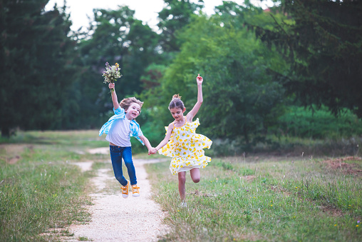 Two happy children with a bouquet of wildflowers running and jumping in a park. Time together.
