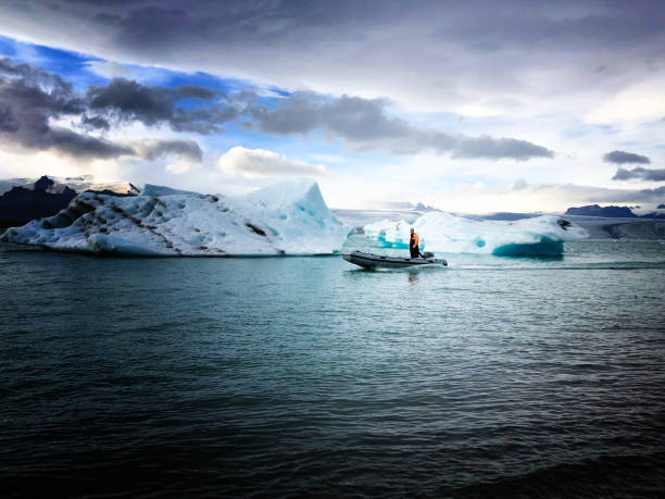 Glacier Lagoon, Iceland: A man in an inflatable raft motoring on Glacier Lagoon, with a dramatic sky background.