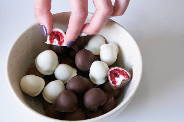 woman's hand choosing and grabbing fresh red and shiny fresh raspberries dipped in homemade black and white chocolate
