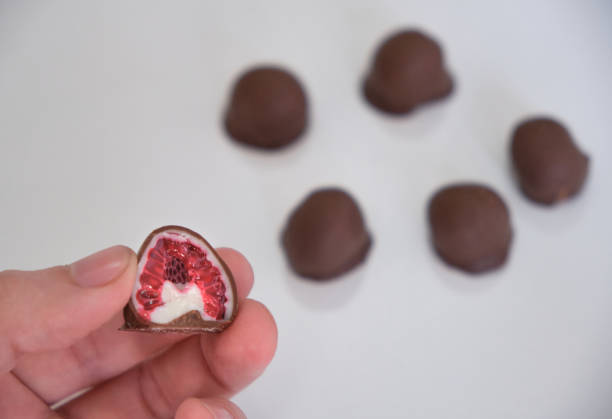woman's hand choosing and grabbing fresh red and shiny fresh raspberries dipped in homemade black and white chocolate