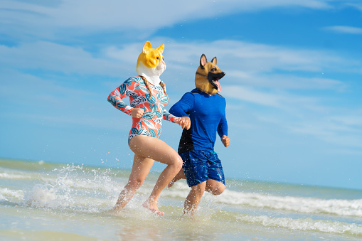 Young couple wearing animal masks running on the beach