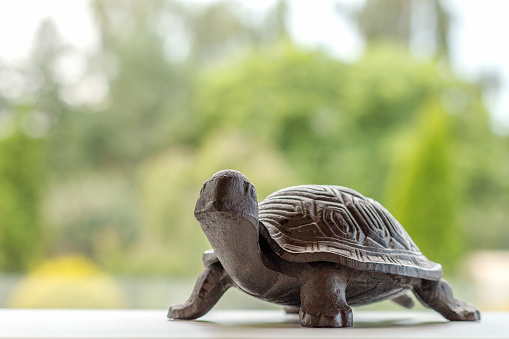 a small brown iron turtle on a white surface by the window in front of a green garden on a sunny summer day, an idea of slow living, enjoying countryside healthy lifestyle, artificial animal pet