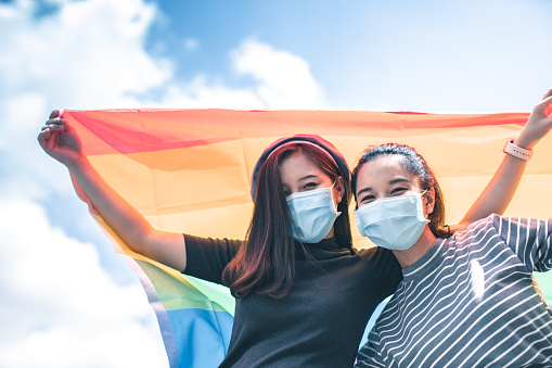 LGBT, portrait of lesbian couple Asian women using lips kissing under rainbow cloth,lesbian concepts.Two pretty women of different race play wrapping in a rainbow flag