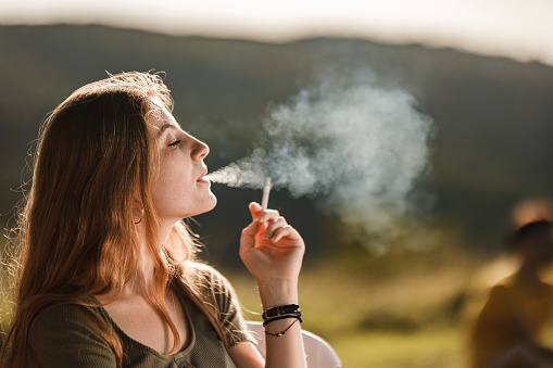 Profile view of a young redhead woman smoking a cigarette in nature. Copy space.