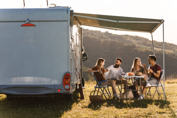 Happy friends communicating at picnic table by the camp trailer in summer day. Young happy couples enjoying while talking at picnic table by the camp trailer. motor home photos stock pictures, royalty-free photos & images