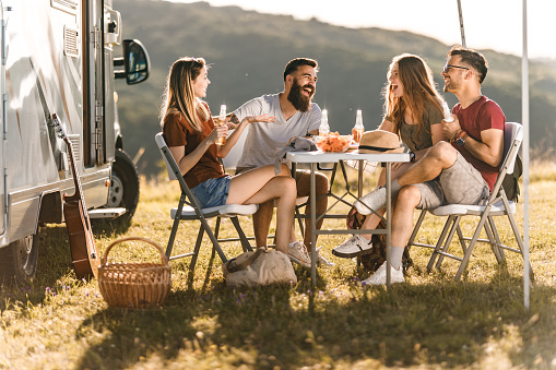 Cheerful friends communicating at picnic table by the camp trailer in summer day.