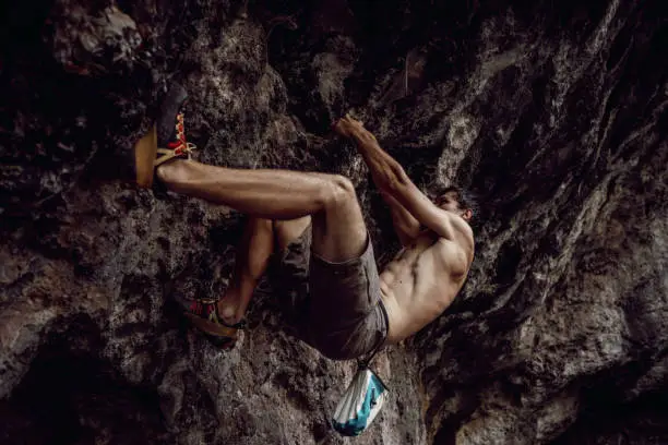 Male climber is climbing up the rock on the extreme terrain.