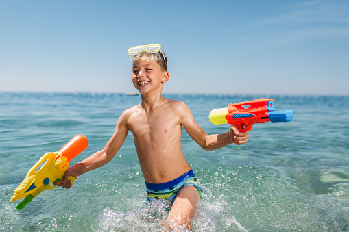 Adorable boys playing with water guns on hot summer day.