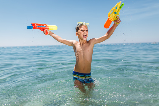 Adorable boys playing with water guns on hot summer day.