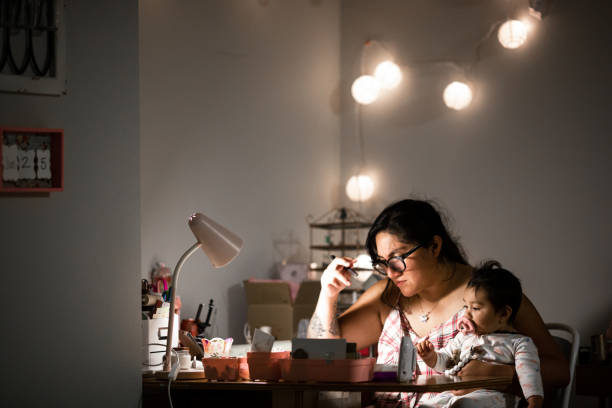 Mother Working From Home at Desk While Holding Baby Daughter - fotografia de stock