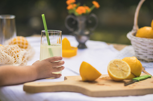 Close up of kid's hand taking a glass of freshly-squeezed lemonade prepared for a sunny day in the backyard.
