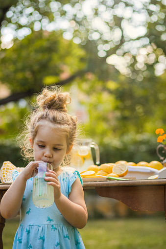 Three quarter length of cute girl standing by the backyard table while enjoying an organic homemade lemon juice.