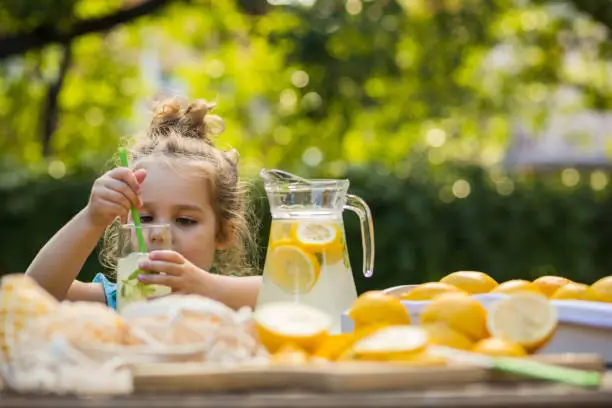 Selective focus, low angle view of cute little girl coming to the table in the backyard to get refreshed  with a delicious lemonade during a summer afternoon.