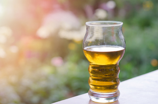 An incomplete glass of cold beer on the table in the garden, blurred background. The concept of relaxing on a summer evening