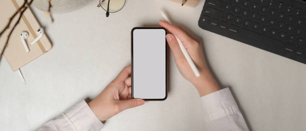 istock Female hands holding smartphone with clipping path on white table 1262593907