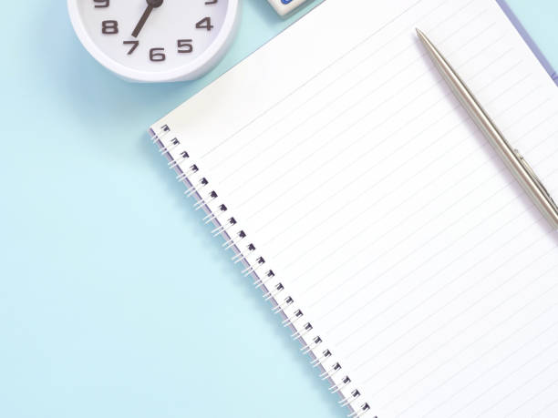 istock Blank notebook and pen with clock at 7:00 am, on blue work place desk table. 1262594130