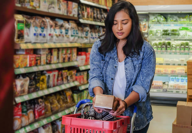 Young millenial reading  food label at the supermarket An attractive young millenial reading food label before buying, at the supermarket nutrition label stock pictures, royalty-free photos & images