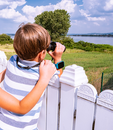 Cute little boy watching through binoculars. Summer vacation in nature