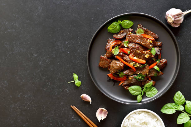 Thai beef stir-fry with pepper and basil on plate Thai beef stir-fry with pepper and basil on plate on a dark stone background with copy space. Top view, flat lay thai culture photos stock pictures, royalty-free photos & images