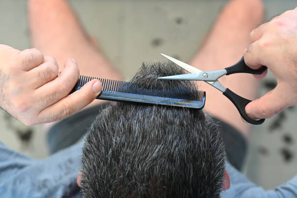 Above view of a man cutting his own hair with comb and scissors.