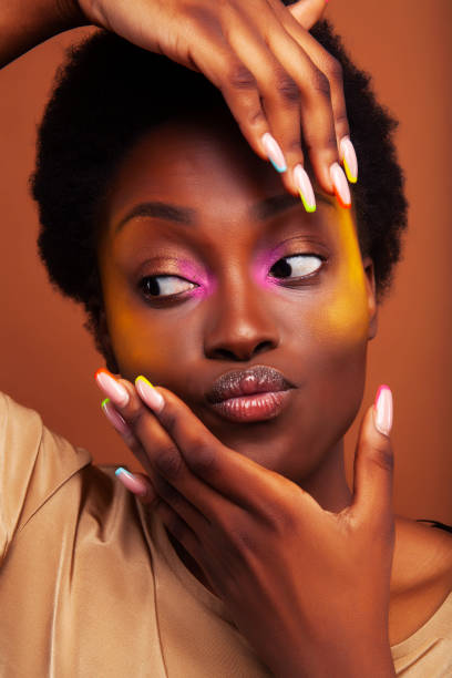 young pretty african girl with bright colorful makeup and manicure posing cheeful on brown background, lifestyle people concept stock photo