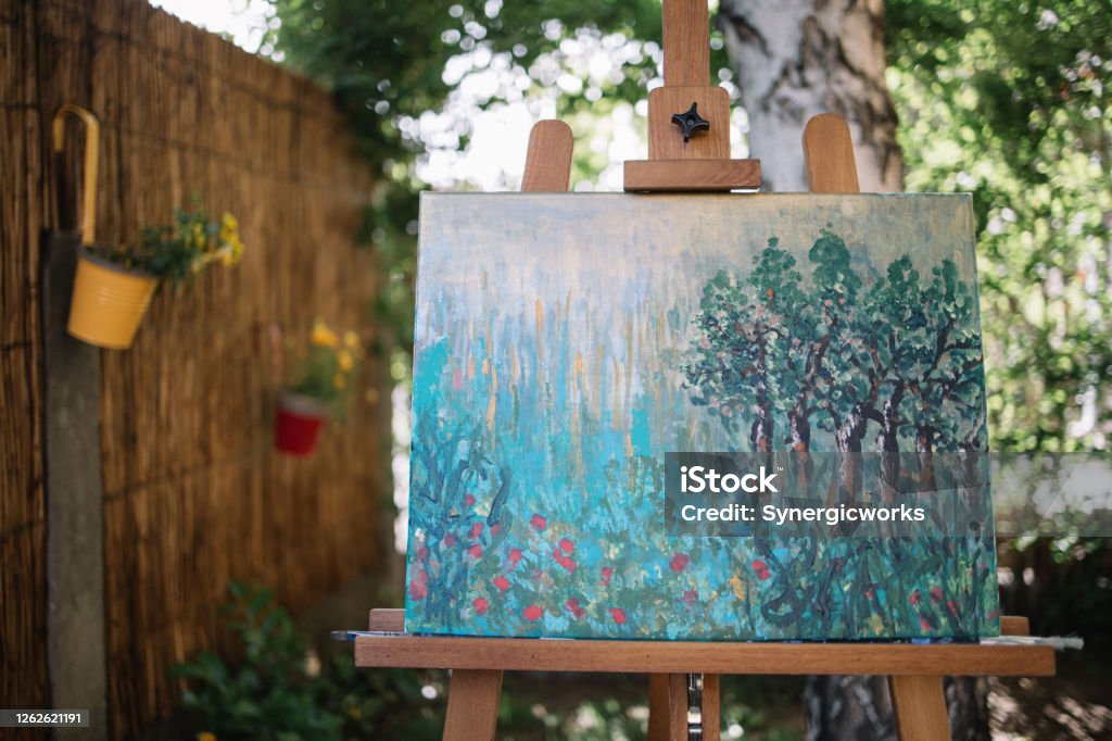Painting on canvas placed on stand in garden Painting on canvas placed on stand in garden. Tripod with watercolor drawing on canvas in backyard with flowers and plants. Art Stock Photo Painting on canvas placed on stand in garden Painting on canvas placed on stand in garden. Tripod with watercolor drawing on canvas in backyard with flowers and plants. Art Stock Photo