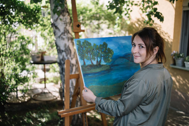 istock Female artist posing while holding painting and looking at camera 1262621687