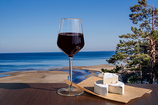 Glass of red wine with brie cheese with view of the White Dune and Baltic see in spring, Latvia. Beach with white sand and blue sea/ocean