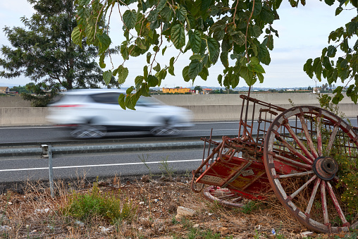 A car at full speed passes in front of an old horse cart