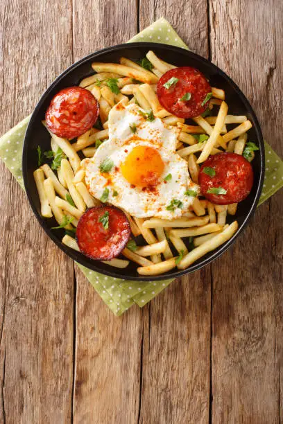 Photo of Spanish cuisine fried egg with fries and chorizo sausage close-up in a plate. vertical top view