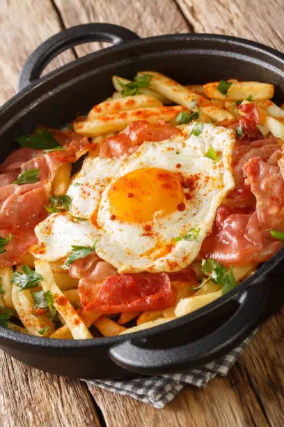 Photo of Huevos rotos con jamon fried egg with fries and ham close-up in a pan. vertical