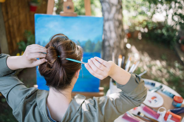 istock Woman making hair bun using paintbrush in yard 1262633129