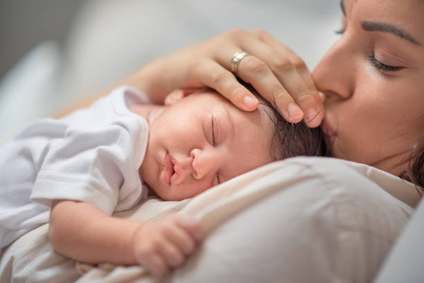 mutter küsst neugeborenen baby jungen kopf, während ihr kind schlafen - lullaby stock-fotos und bilder