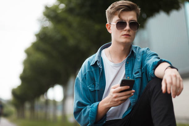 istock Handsome young guy sitting on a bench with a smartphone on the internet 1262633445