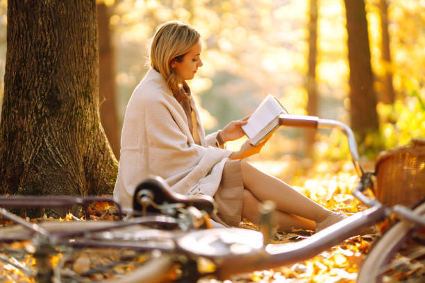 istock Beautiful young woman sitting on a fallen autumn leaves in a park, reading a book. 1262639607